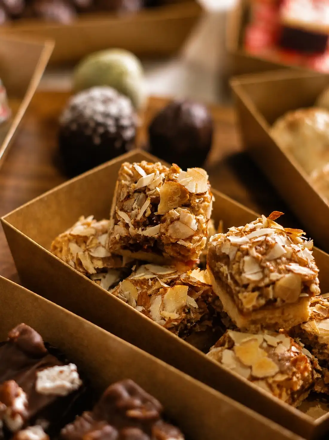An open kraft treat box packed with almond slices, truffles and squares of chocolate.