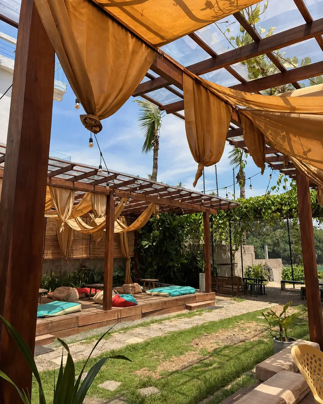 The garden pergola at Kāffi Ahangama, ochre canvas drapes tied back over a raised timber deck laid with cushions.
