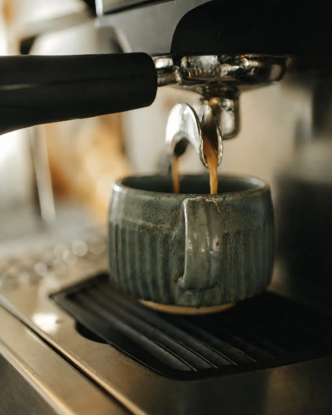 Espresso pouring from the group head into a ribbed blue-glazed stoneware cup.