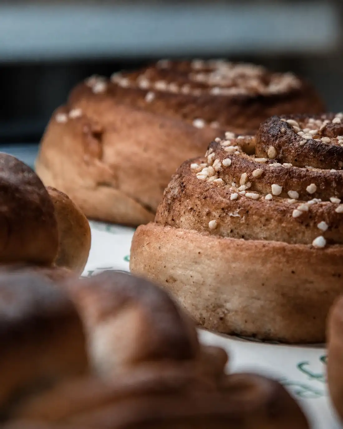 Cinnamon buns cooling on paper, their tops crusted with Nordic pearl sugar.