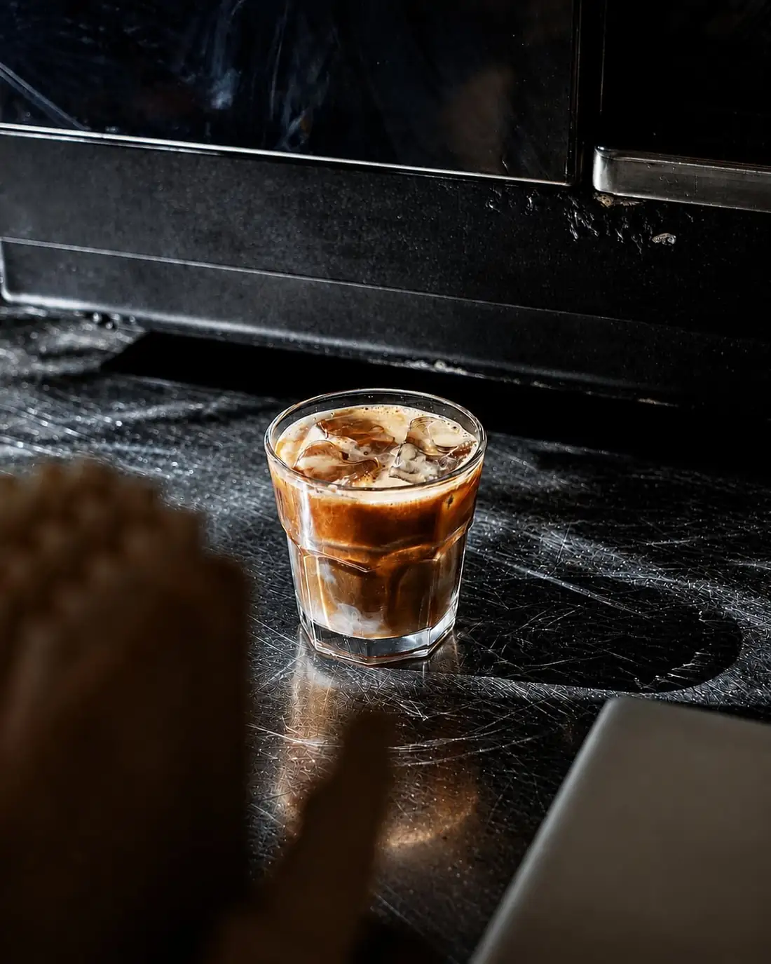 An iced espresso in a heavy glass on a steel counter.